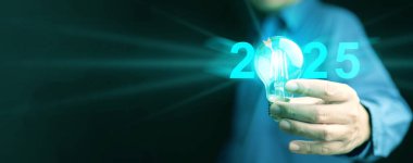 2025 fikir ve amaç. Bir adam, önümüzdeki yıl iş, teknoloji veya özel hayat için hedef ve stratejik planı temsil eden sanal dart ikonuyla aydınlatma ampulünü elinde tutuyor.