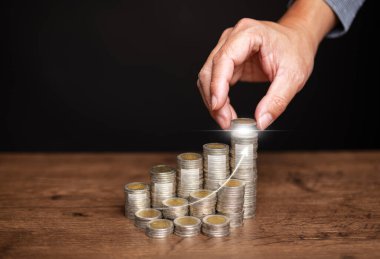 Tasarruf, yatırım ve finansal planlama. Bir adamın eli, madeni büyümeyi ve zenginliği sembolize eden yükselen oklu bir çizgiyle bozuk parayı yığının üzerine yerleştiriyor..