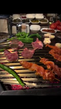 meat vegetables mushrooms lie on a barbecue and cook, a person turns vegetables and meat on a barbecue with tongs