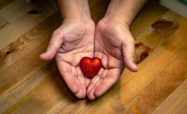 Ahşap arka planda kırmızı kalbi tutan eller