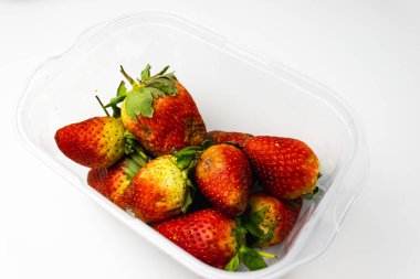 Beyaz arka planda cam bir kasede taze çilekler.