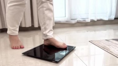 Banyo tartısında kendini tartan bir kadın, sağlık kontrolü, kendini tartmaya çalışan ve siyah tartıya mezura fırlatan genç bir kadının yakın çekimi. Yüksek kalite 4k görüntü