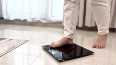 Banyo tartısında kendini tartan bir kadın, sağlık kontrolü, kendini tartmaya çalışan ve siyah tartıya mezura fırlatan genç bir kadının yakın çekimi. Yüksek kalite 4k görüntü