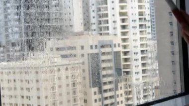 Camları siliyorum. Evde temizlik hizmeti. Sabun solüsyonu pencereye sıçradı. Temiz cam. Camları silmek için kazıyıcı. Ev hanımı pencereyi temizler. Yatay video. Yüksek kalite 4k görüntü