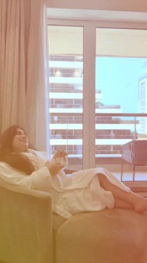 Genç bir kadın elinde tabletle evde dinleniyor.