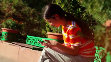 Parkta oturan kız cep telefonu kullanıyor.