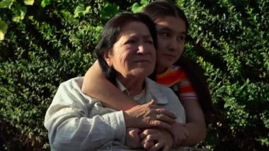 Genç bayan bakıcı, yaşlı bir kadını tekerlekli sandalyeyle şehir caddesinde gezdirirken ve yaz günü yürürken onunla sohbet ederken. Tekerlekli sandalyedeki engelli büyükanneyle ilgilenen genç kız, yaşlı nesle bakıyor.. 