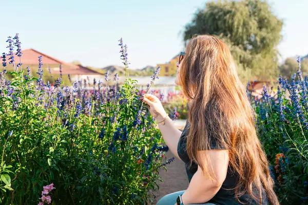 Çiçek açan bahar bahçesinde kokunun tadını çıkaran genç bir kadın. Gençlik, aşk, moda ve yaşam tarzı kavramı. Yüksek kalite fotoğraf