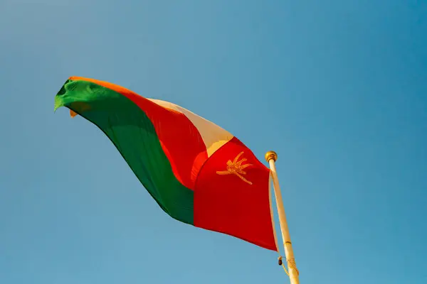 Umman bayrağı rüzgarda, ulusal gurur ve kimliği simgeleyen canlı mavi gökyüzüne karşı zarif bir şekilde dalgalanıyor. Yüksek kalite fotoğraf