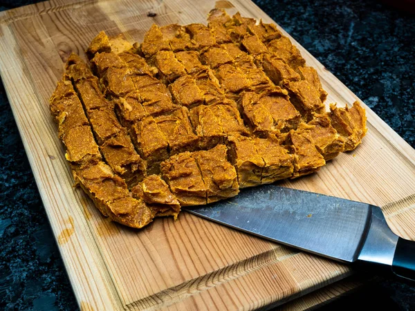 Homemade dog treats made of pumpkin, arranged on a wooden cutting block alongside a knife. The treats are a healthy and nutritious snack for dogs and are often preferred by pet owners who prefer natural ingredients.