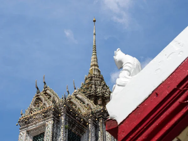 Bangkok, Tayland 'daki Wat Arun Tapınağı' nın kulesi, kırmızı ve beyaz çatı detaylarıyla süslenmiş mavi gökyüzüne karşı dimdik ayakta duruyor. Karmaşık şablonlar ve detaylı işçilik tapınağın zengin kültürel mirasını gösteriyor.