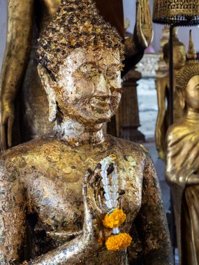 Tanrısallığı, Tayland 'ın Bangkok kentindeki Wat Arun Tapınağı' nda, Phuang Malai adlı canlı sarı çiçekle süslenmiş altın Buda heykelinin bu çarpıcı yakın planına bir göz atın. Karmaşık detaylar ve ilahi aura seni büyüleyecek..