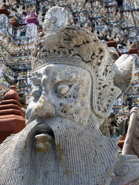 Bangkok, Tayland 'daki ikonik Şafak Tapınağı, Wat Arun Tapınağı' ndaki koruyucu bir heykelin görkemli yüzünün yakın çekimi. Karmaşık detaylar ve güçlü bir ifadeyle heykel bir güç ve koruma hissi yayarak onu zamansız bir yapı haline getiriyor.
