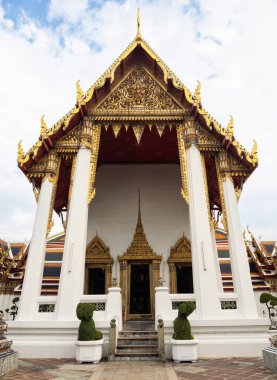 Bu fotoğraf Bangkok, Tayland 'daki Wat Pho kompleksinin içindeki karmaşık altın çatılı küçük bir tapınak binasını çekiyor. Tapınağın tasarladığı karmaşık detaylar ve canlı renkler zengin tarihi gözler önüne seriyor.