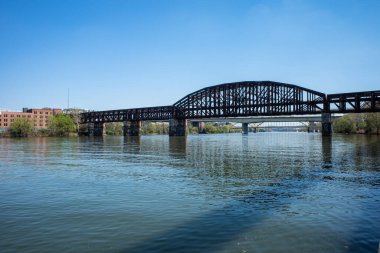 Pittsburgh 'da güneşli bir gökyüzünün altında Allegheny Nehri boyunca uzanan bir demiryolu köprüsü ve diğer geçitler vardır..