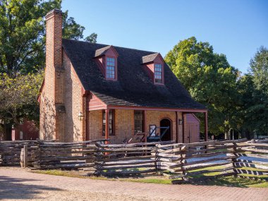 Güneşli bir günde Williamsburg, Virginia, ABD 'de mavi gökyüzü tahta bir çitle tamamlanmış tarihi bir kırmızı tuğla bina duruyor..