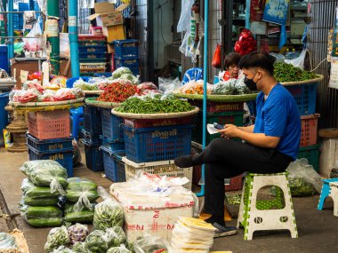 Kırmızı ve yeşilin tonlarında iki baharatlı biber satıcısı, Bangkok 'taki açık hava pazarında oturuyorlar ve müşteri umuyorlar..