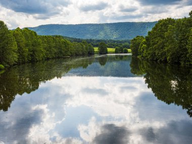 Virginia, ABD 'deki Shenandoah Nehri' nin güney çatalı, ağaçlar, gökyüzü, bulutlar ve uzak dağları yansıtan sakin sularla övünür..