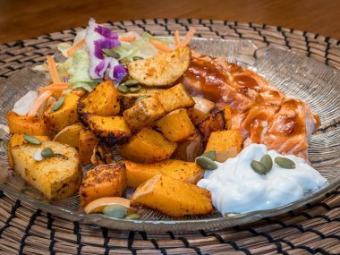 Fırında kızartılmış patatesler, tavuk, salata ve kremalı taze krema içeren sağlıklı bir akşam yemeği bambu bir tabak üzerinde güzelce sunuluyor..