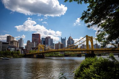 Bathed in the warm sunlight of a Pittsburgh summer day, the yellow Rachel Carson Bridge stands out against the backdrop of a clear blue sky adorned with fluffy white clouds. clipart