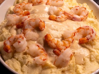 A close-up of a seafood casserole dish, showcasing the rich texture of mashed potatoes contrasting with plump shrimp glistening in a creamy white wine sauce. clipart