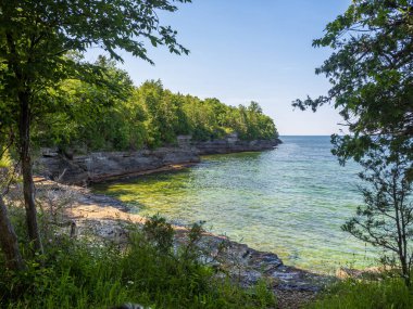 Uçurumlar ve yemyeşil bitki örtüsü New York eyaletindeki Ontario Gölü 'nün berrak suları boyunca uzanan sakin bir körfez boyunca uzanır. Uçsuz bucaksız mavi bir gökyüzü ve sakin bir ufuk çizgisi altında..
