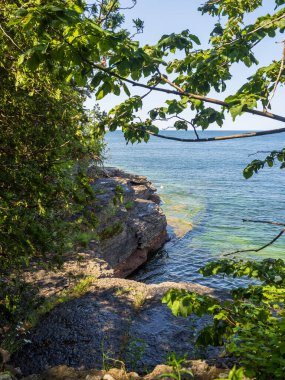 Uçurumlar ve yemyeşil bitki örtüsü New York eyaletindeki Ontario Gölü 'nün berrak sularının yanında duruyor. Arka planda çarpıcı mavi bir gökyüzü ve sakin bir ufuk çizgisi var..
