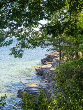 Uçurumlar ve yemyeşil bitki örtüsü New York eyaletindeki Ontario Gölü 'nün berrak sularının yanında duruyor. Arka planda çarpıcı mavi bir gökyüzü ve sakin bir ufuk çizgisi var..
