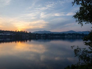 Nefes kesen bir günbatımı, Placid Gölü 'nün üzerine altın renkler saçar. Aynalı Göl boyunca uzanan Adirondack Dağları' nın huzur dolu güzelliğini yansıtır. New York 'un kuzeyinin huzurlu özünü yakalar..