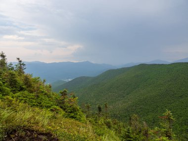 A breathtaking view from Cascade Mountain's summit, where rays of light pierce through heavy clouds, illuminating the Adirondacks in New York State. clipart