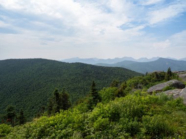 Stunning view from the summit of Cascade Mountain, Lake Placid, showcasing rugged rocks in the foreground and the expansive Adirondack forest landscape beyond. clipart