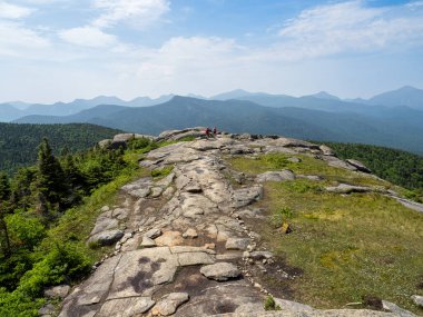 Kırmızı sırt çantalı iki yürüyüşçü Cascade Dağı 'ndan mavi gökyüzünün altındaki büyüleyici Adirondack Dağları' na doğru ilerliyorlar..