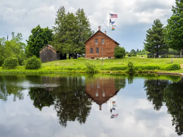 stock image The John Brown Farmhouse reflects beautifully in the mirror-like pond, framed by waving American and rainbow flags, creating a vibrant and peaceful scene.