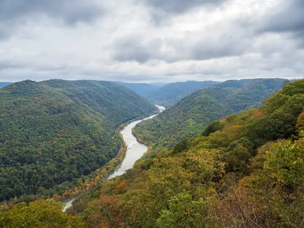 Grandview Rim, New River Gorge Ulusal Parkı, Batı Virginia 'da bulutlu bir gökyüzü altında büyüleyici ve karamsar bir atmosfer yaratarak canlı sonbahar renkleri sergiliyor..