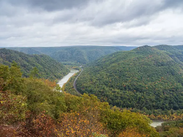 Grandview Rim, New River Gorge Ulusal Parkı, Batı Virginia 'da bulutlu bir gökyüzü altında büyüleyici ve karamsar bir atmosfer yaratarak canlı sonbahar renkleri sergiliyor..
