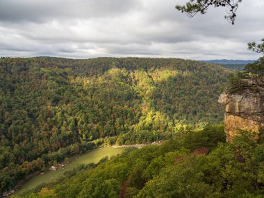 Güneş ışığı, New River Gorge Ulusal Parkı, Batı Virginia 'daki suların üzerindeki rengarenk dağ yamacını vurgular ve çarpıcı bir sonbahar manzarası yaratır..