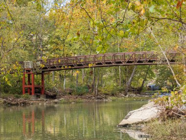 The red foundation of the bridge at Sandstone Falls in New River Gorge National Park stands out against the shimmering water, with vibrant autumn foliage reflecting beautifully on the surface. clipart