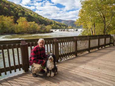 Kırmızı oduncu ceketi giymiş bir Bernedoodle köpeği ve sahibi, Batı Virginia, New River Gorge Ulusal Parkı, Sandstone Falls 'un engebeli güzelliğini....