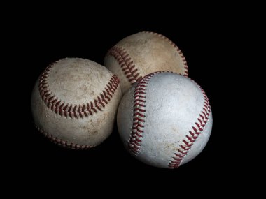 Üç beysbol topundan oluşan çarpıcı bir düzenleme, parlak siyah bir arka planda izole edilmiş, dokularını, dikişlerini ve klasik tasarımlarını gözler önüne seriyor..