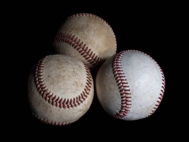 Üç beysbol topundan oluşan çarpıcı bir düzenleme, parlak siyah bir arka planda izole edilmiş, dokularını, dikişlerini ve klasik tasarımlarını gözler önüne seriyor..