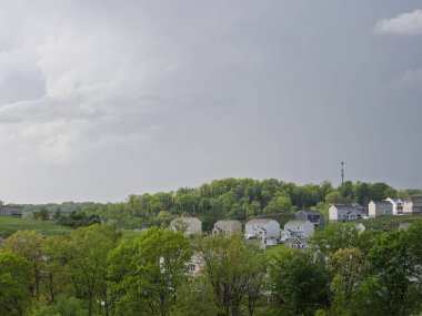 Evler, Pittsburgh yakınlarındaki bir yerleşim bölgesinde yemyeşil ağaçlar ve bulutlu bir gökyüzünün altında yuvarlanan tepelerle çevrilidir..