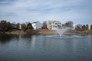 Ashburn, Virginia kıyı şeridinde bir çeşme ve konut evlerinin yer aldığı bir banliyö gölü manzarası.
