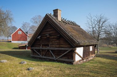 Ayırt edici sazdan çatısı ve tuğladan bacası olan geleneksel bir ahşap kulübe İsveç 'in Haessleholm kentindeki çimenli bir tepede duruyor..