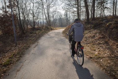 İsveç 'in Haessleholm şehrinde çıplak kış ağaçlarıyla çevrili, dolambaçlı bir patika boyunca bisiklet süren bir insan..