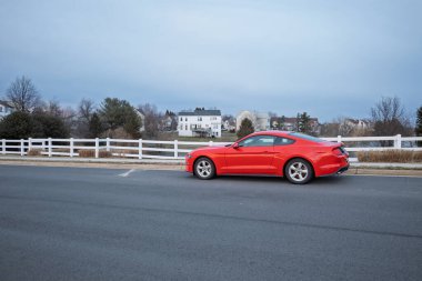 Çarpıcı kırmızı bir Ford Mustang banliyö sokağında, Ashburn, Virginia 'da evleri ve beyaz çitleri olan.