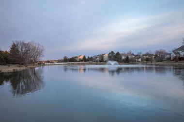 Kış güneşinin ilk ışıkları donmuş bir göletin üzerine altın bir parıltı saçar. Ashburn, Virginia 'da bir çeşme ile. Huzurlu ve manzaralı bir sabah manzarası yaratır..