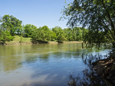 Potomac Nehri, Paw Paw, Batı Virginia 'da açık mavi bir gökyüzünün altında yemyeşil bir ağaç hattının yanından akar..
