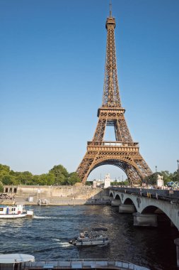Muhteşem Eyfel Kulesi Fransa 'nın başkenti Paris' te güneşli bir günde Seine Nehri 'nin sakin sularında yüzen teknelerle Pont d' elna Köprüsü 'ne bakıyor..