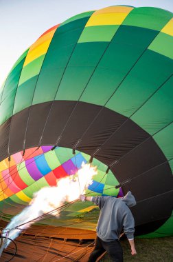 Close up of hot air balloon burner flame and colorful hot air balloon. Person holding stripes of air balloon.