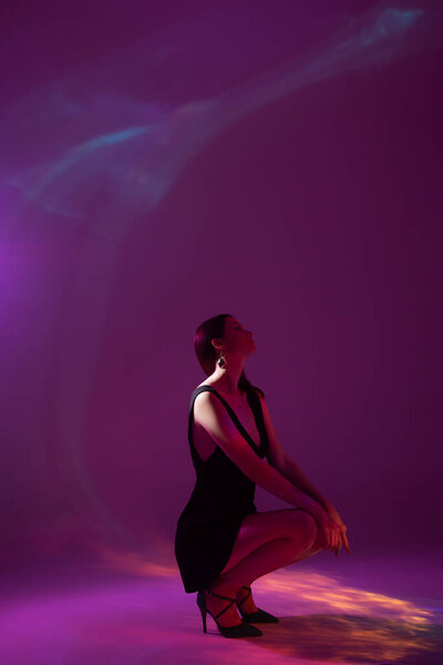 Portrait of young woman in black dress with neon light reflection on body over multicolored background